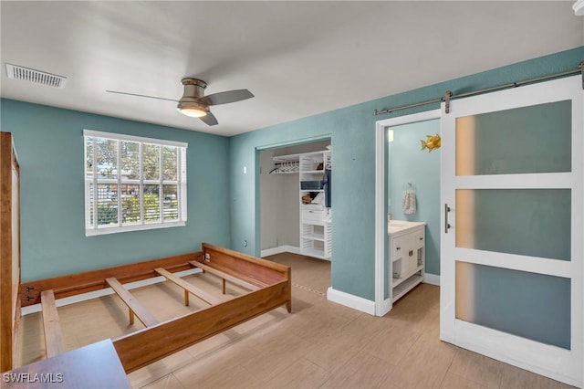 bedroom with light wood finished floors, a closet, visible vents, a barn door, and baseboards