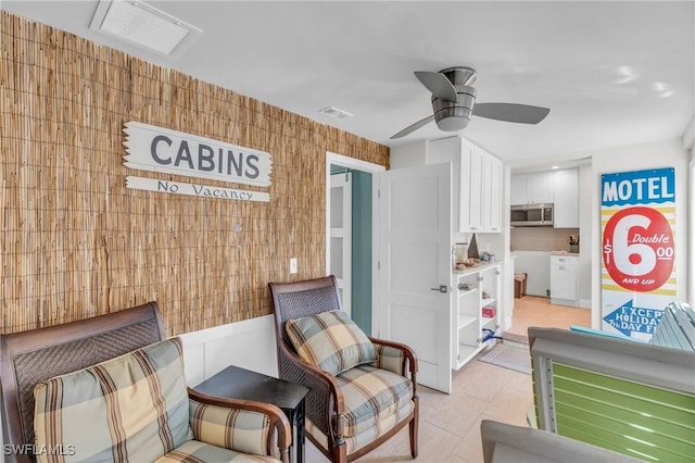 living area with ceiling fan, a wainscoted wall, visible vents, and wallpapered walls