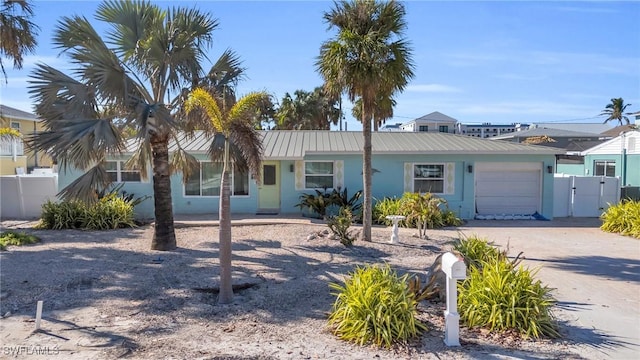 ranch-style house featuring stucco siding, an attached garage, fence, metal roof, and driveway