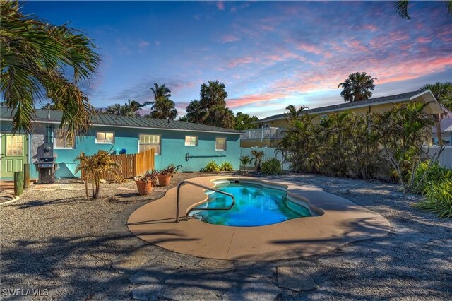 pool at dusk featuring a patio and grilling area