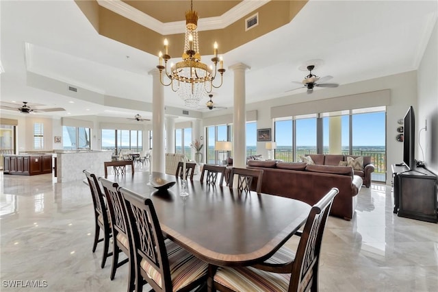 dining space with a raised ceiling, ornamental molding, ceiling fan with notable chandelier, and ornate columns