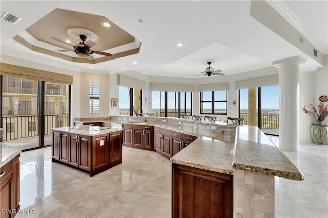 kitchen featuring a spacious island, light stone countertops, a raised ceiling, kitchen peninsula, and ornate columns