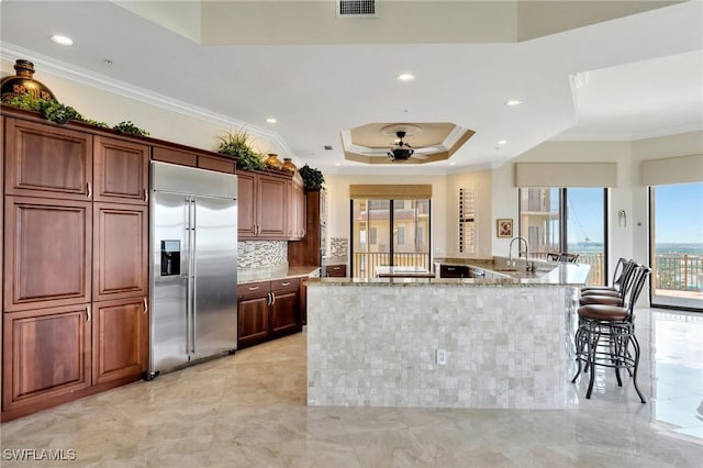 kitchen featuring light stone counters, stainless steel built in refrigerator, a tray ceiling, decorative backsplash, and ornamental molding