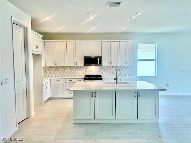 kitchen featuring an island with sink, sink, white cabinets, decorative backsplash, and stove