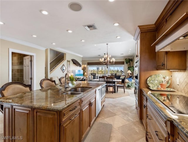 kitchen featuring sink, hanging light fixtures, an island with sink, a chandelier, and decorative backsplash