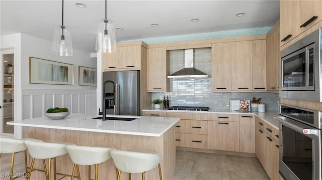 kitchen featuring a kitchen island with sink, a breakfast bar area, wall chimney exhaust hood, light brown cabinetry, and stainless steel appliances