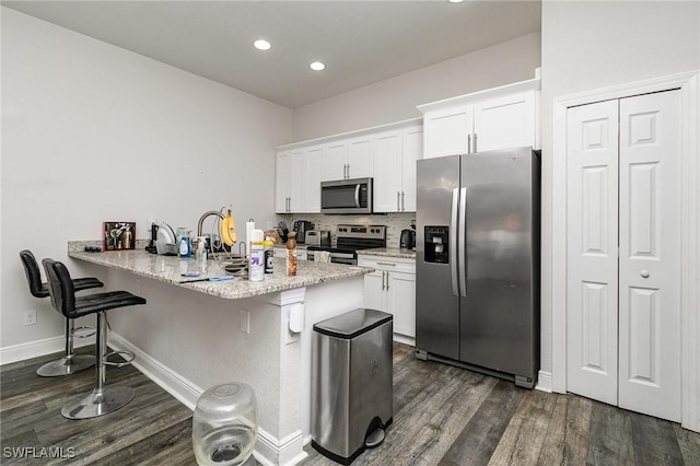 kitchen with a breakfast bar, dark hardwood / wood-style floors, white cabinetry, kitchen peninsula, and stainless steel appliances