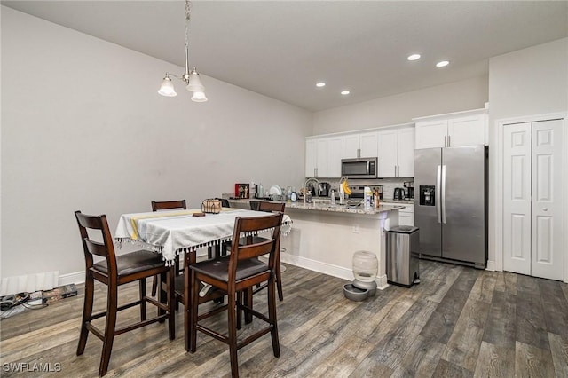 kitchen with light stone countertops, stainless steel appliances, dark wood-type flooring, white cabinetry, and a breakfast bar area