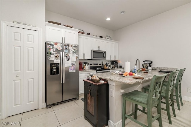 kitchen featuring decorative backsplash, appliances with stainless steel finishes, white cabinetry, a breakfast bar area, and light tile patterned flooring