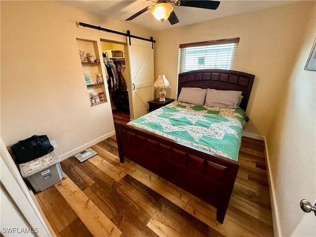 bedroom featuring a walk in closet, hardwood / wood-style flooring, a closet, ceiling fan, and a barn door