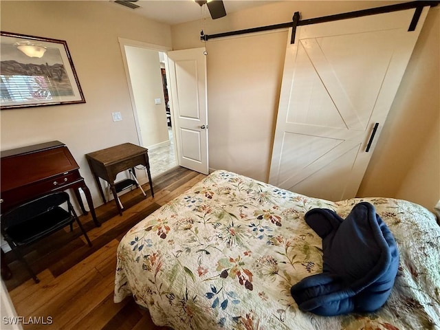 bedroom featuring ceiling fan, a barn door, and dark wood-type flooring