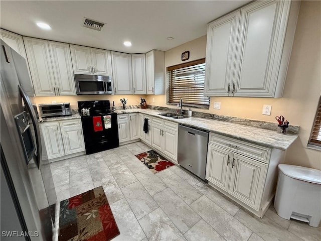 kitchen with light stone countertops, sink, stainless steel appliances, and white cabinetry