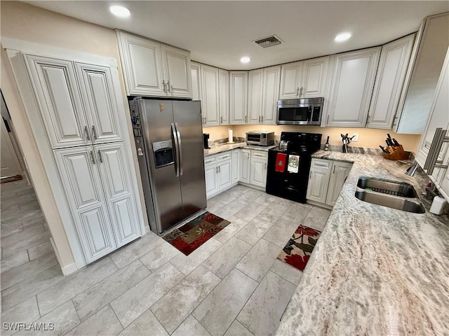 kitchen with light stone countertops, stainless steel appliances, white cabinets, and sink