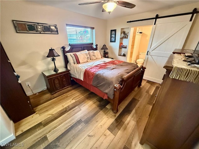 bedroom featuring ceiling fan, a barn door, wood-type flooring, and ensuite bath