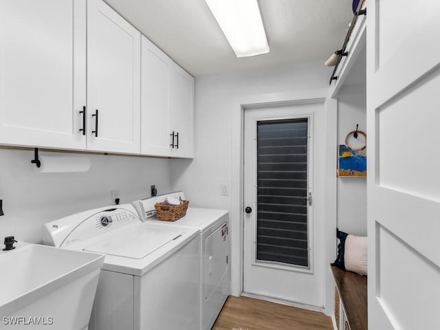 clothes washing area with washer and dryer, light hardwood / wood-style flooring, cabinets, and sink