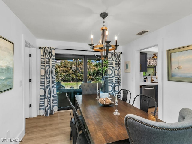 dining area with light wood-type flooring, sink, and an inviting chandelier