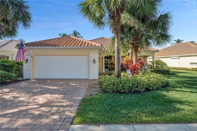 mediterranean / spanish home with an attached garage, a tile roof, decorative driveway, stucco siding, and a front lawn