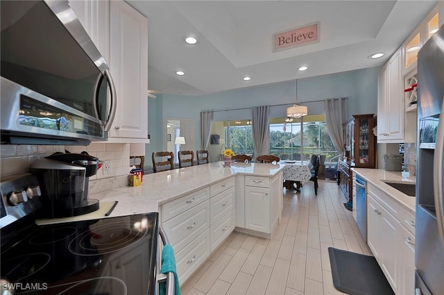 kitchen with kitchen peninsula, light stone counters, stainless steel appliances, pendant lighting, and white cabinetry