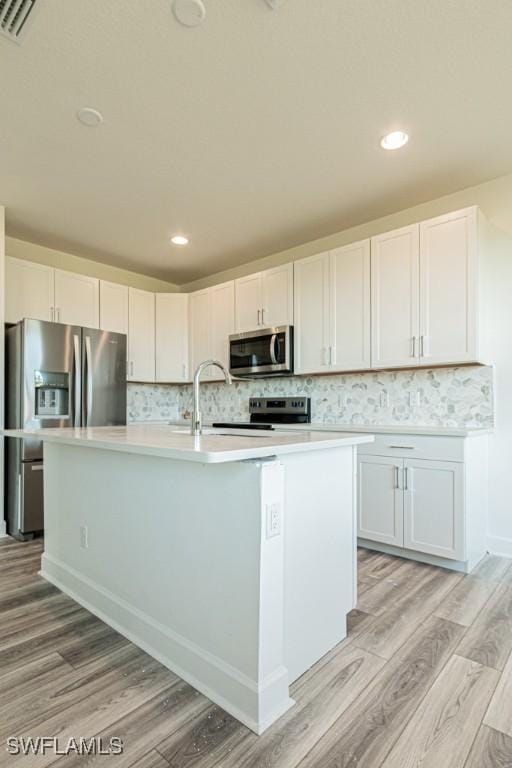 kitchen featuring white cabinets, a center island with sink, stainless steel appliances, and light hardwood / wood-style flooring