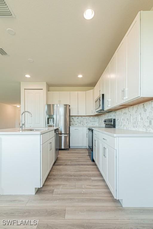 kitchen featuring white cabinetry, sink, stainless steel appliances, light hardwood / wood-style flooring, and decorative backsplash