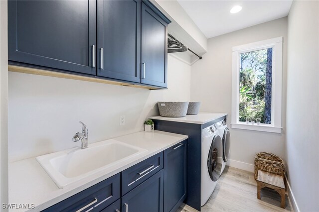 laundry room with washer and dryer, sink, cabinets, and light hardwood / wood-style flooring