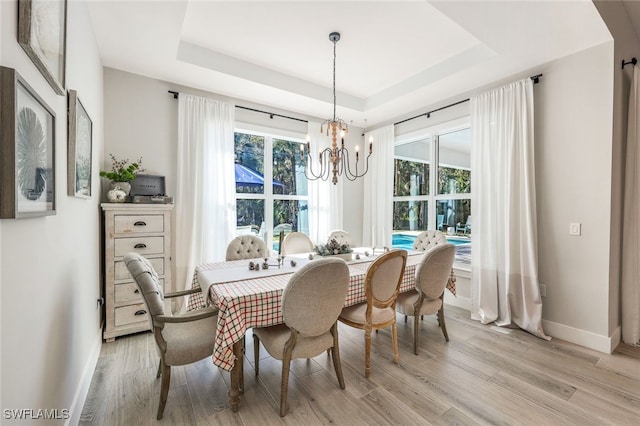 dining room featuring a notable chandelier, light hardwood / wood-style floors, and a tray ceiling