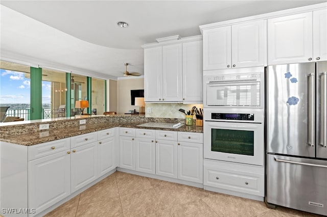 kitchen with white cabinetry, dark stone countertops, and white appliances