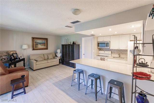 3 Bob O Link Ct Unit 3B, Naples, FL 34105 - kitchen featuring stainless steel microwave, white range with electric cooktop, a peninsula, a breakfast bar, and white cabinetry