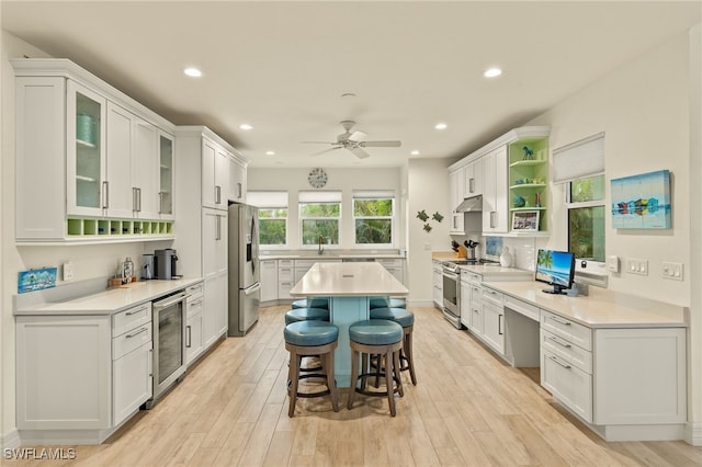 kitchen featuring a kitchen breakfast bar, light wood-type flooring, stainless steel appliances, white cabinets, and wine cooler