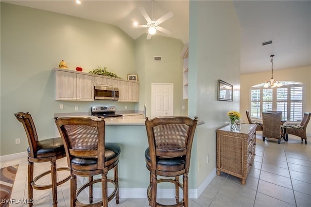 kitchen with kitchen peninsula, appliances with stainless steel finishes, ceiling fan with notable chandelier, light tile patterned floors, and high vaulted ceiling