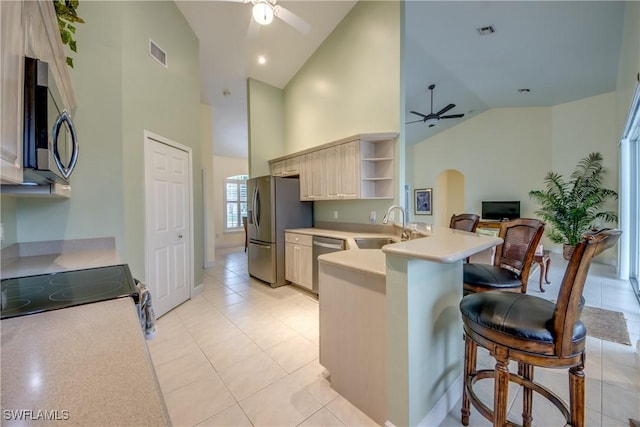 kitchen with kitchen peninsula, a kitchen breakfast bar, stainless steel appliances, sink, and high vaulted ceiling