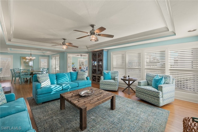 living room with a raised ceiling, crown molding, wood-type flooring, and ceiling fan with notable chandelier