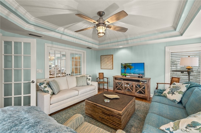 living room with a raised ceiling, ceiling fan, and crown molding