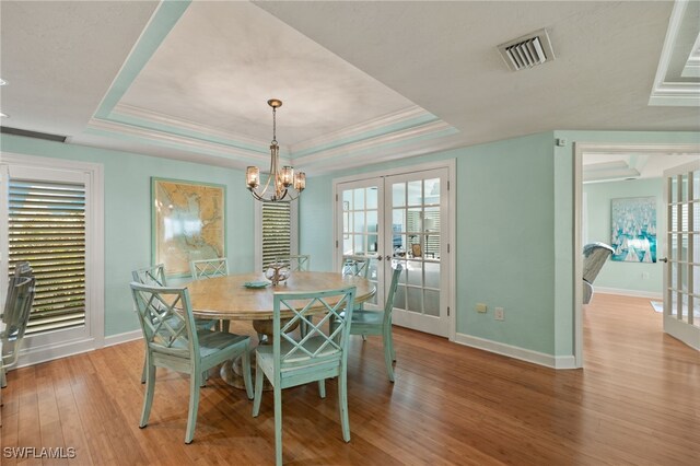 dining space with a raised ceiling, french doors, an inviting chandelier, and light hardwood / wood-style flooring