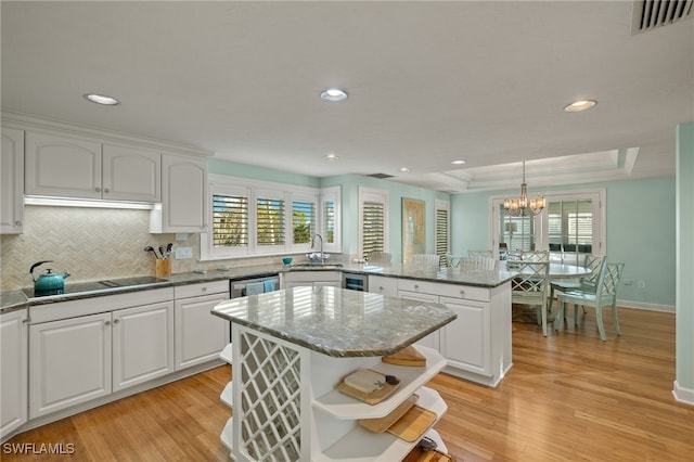 kitchen featuring a center island, black electric stovetop, white cabinets, and decorative light fixtures