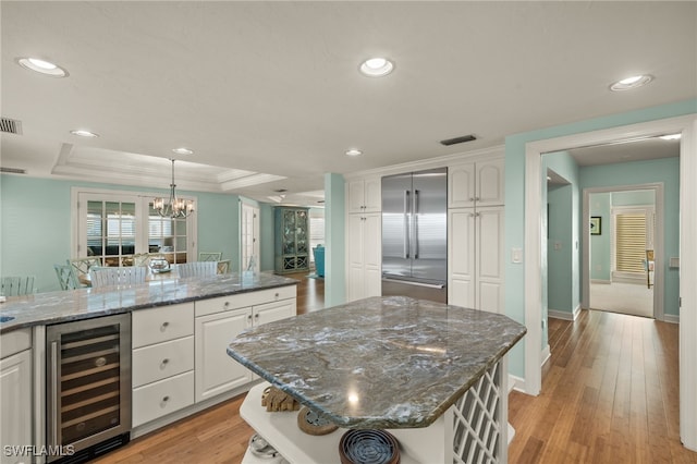 kitchen featuring a tray ceiling, white cabinets, beverage cooler, and stainless steel built in refrigerator