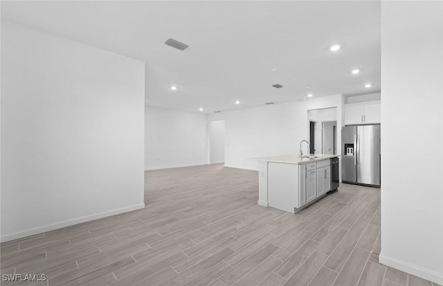 kitchen featuring a center island with sink, sink, light wood-type flooring, appliances with stainless steel finishes, and white cabinetry