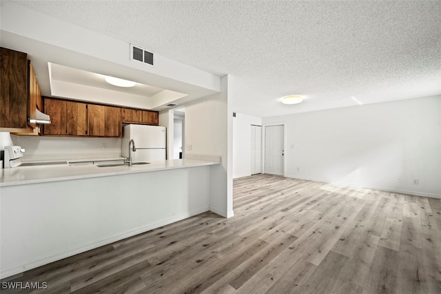 kitchen with range, a textured ceiling, white fridge, light wood-type flooring, and kitchen peninsula