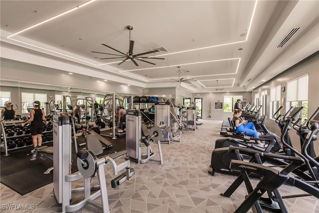 exercise room featuring a tray ceiling, ceiling fan, and light colored carpet