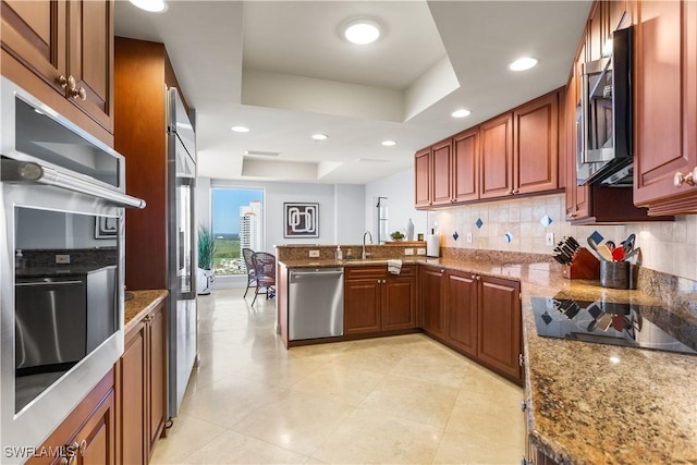 kitchen featuring appliances with stainless steel finishes, tasteful backsplash, a tray ceiling, light stone counters, and kitchen peninsula