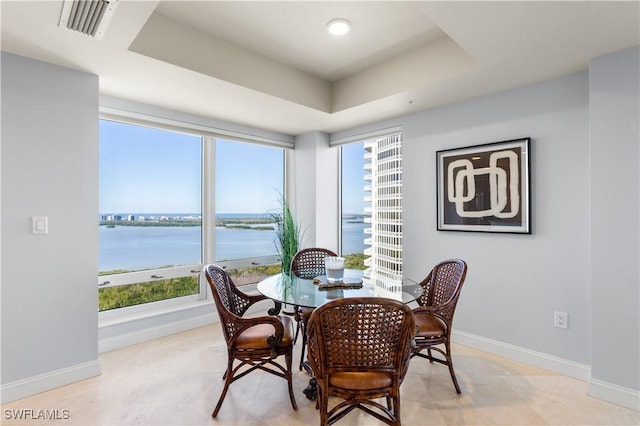 dining area featuring a raised ceiling, plenty of natural light, and a water view