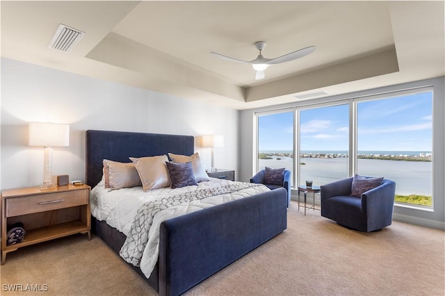 carpeted bedroom with a raised ceiling, ceiling fan, a water view, and multiple windows