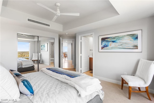 carpeted bedroom featuring a tray ceiling, ceiling fan, a closet, and ensuite bathroom