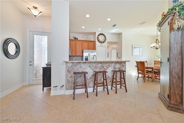 kitchen with stainless steel fridge, a breakfast bar, light tile patterned floors, and hanging light fixtures