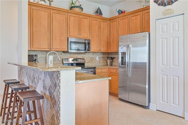 kitchen featuring backsplash, light stone counters, appliances with stainless steel finishes, a kitchen bar, and kitchen peninsula