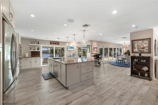 kitchen with a sink, visible vents, hanging light fixtures, appliances with stainless steel finishes, and a center island with sink