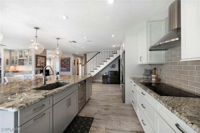 kitchen featuring wall chimney exhaust hood, a center island with sink, white cabinetry, and a sink