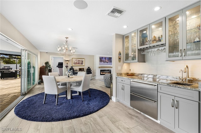 kitchen featuring visible vents, glass insert cabinets, light stone counters, gray cabinets, and a sink