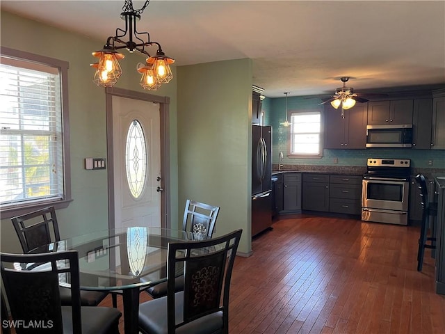 dining area featuring ceiling fan with notable chandelier, dark wood-type flooring, and sink