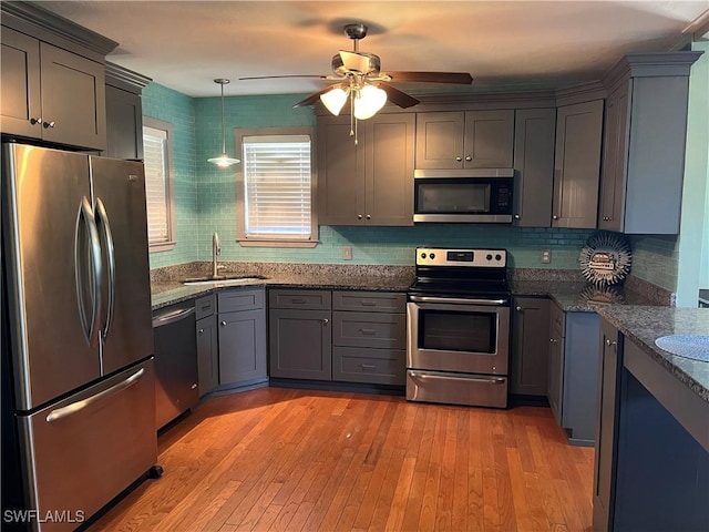 kitchen with decorative light fixtures, stainless steel appliances, light hardwood / wood-style floors, and sink